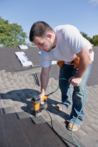 Professional roofer with nail gun installing new shingles